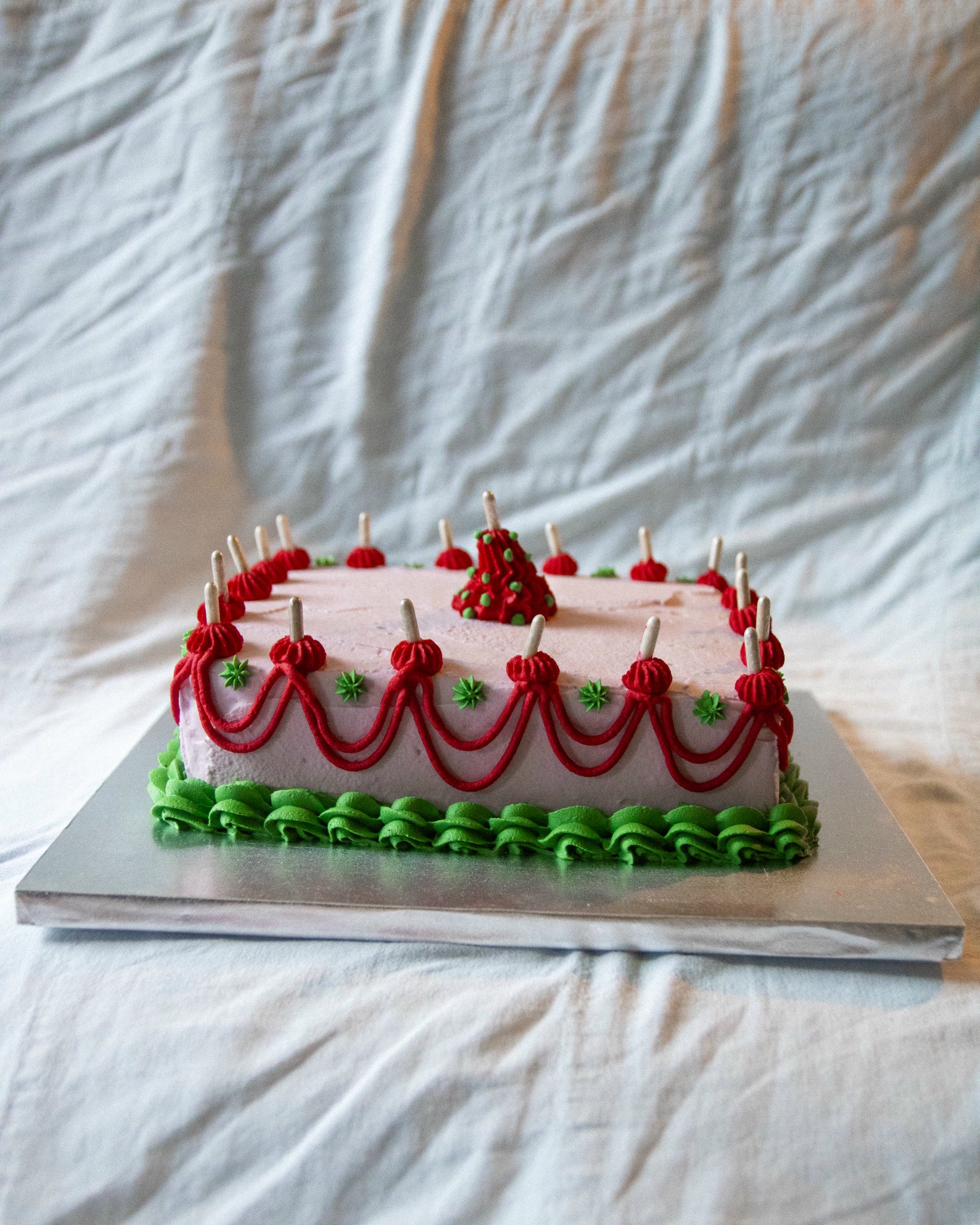 Celebration cake — pink rectangular sheet cake with red swag piping, green ruffle border and candles
