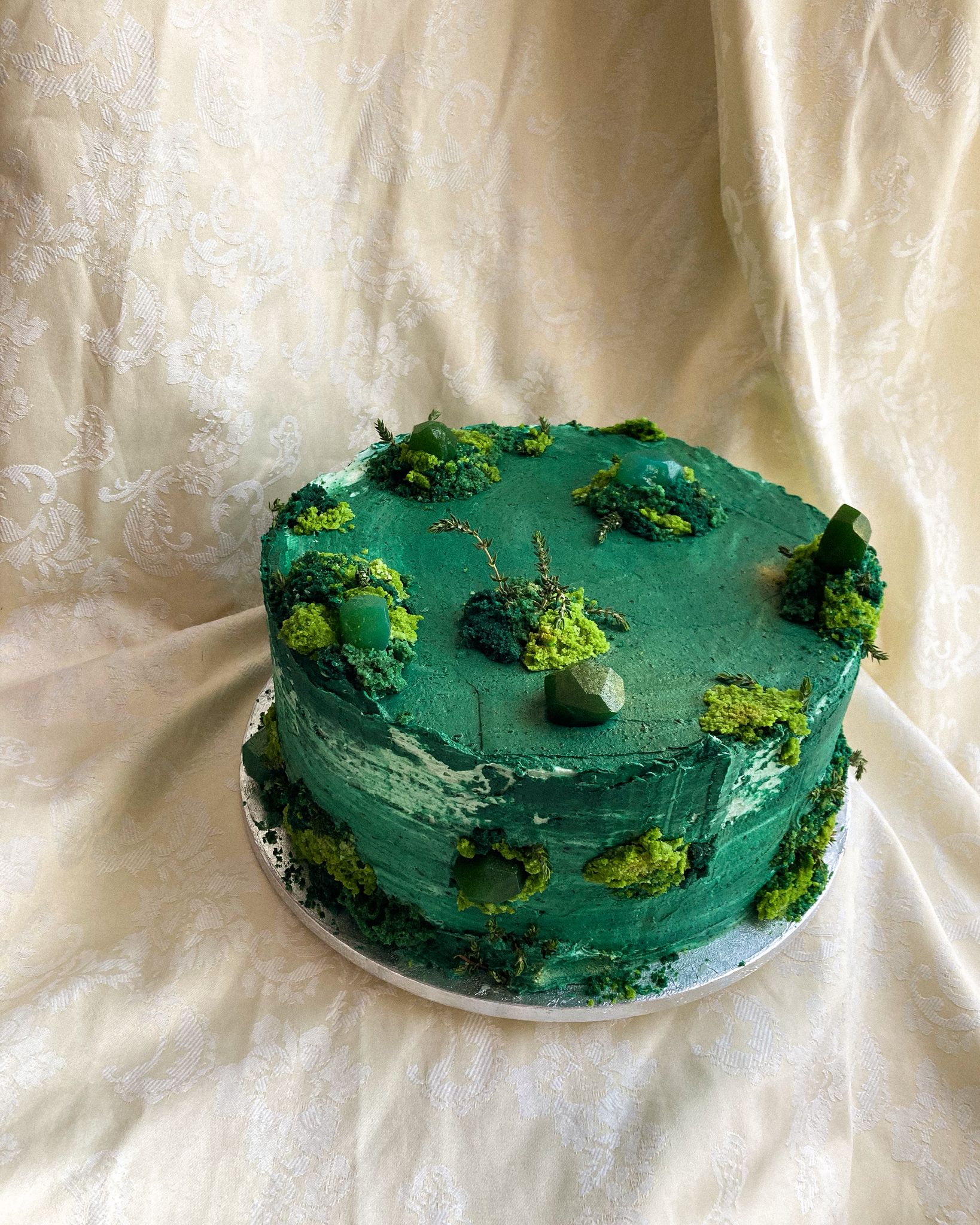 Celebration cake — deep green buttercream with moss-like cake crumb texture, green aventurine crystals and fresh herb sprigs